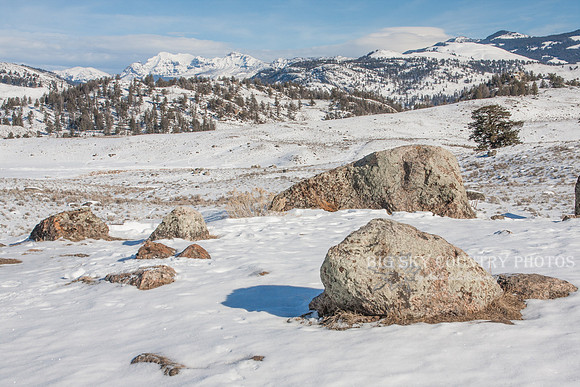 winter scene with mountain peaks in the distance and sagebrush and boulders in foreground