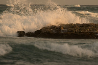 Waves lit by the warm light of the setting sun crash against the rocks off the beach at the Zamas Hotel