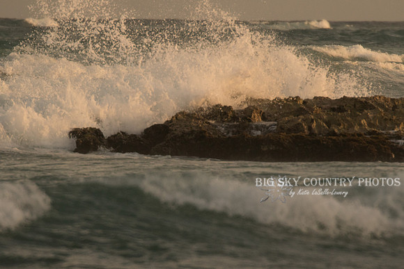 Waves lit by the warm light of the setting sun crash against the rocks off the beach at the Zamas Hotel